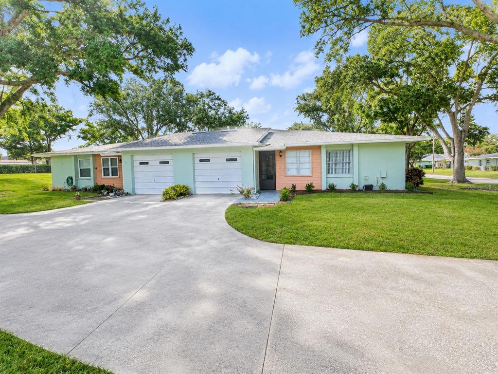 A single-story duplex with a light green exterior, two garage doors, and a concrete driveway — 1131 ORANGE TREE CIRCLE W UNIT C, PALM HARBOR, FL