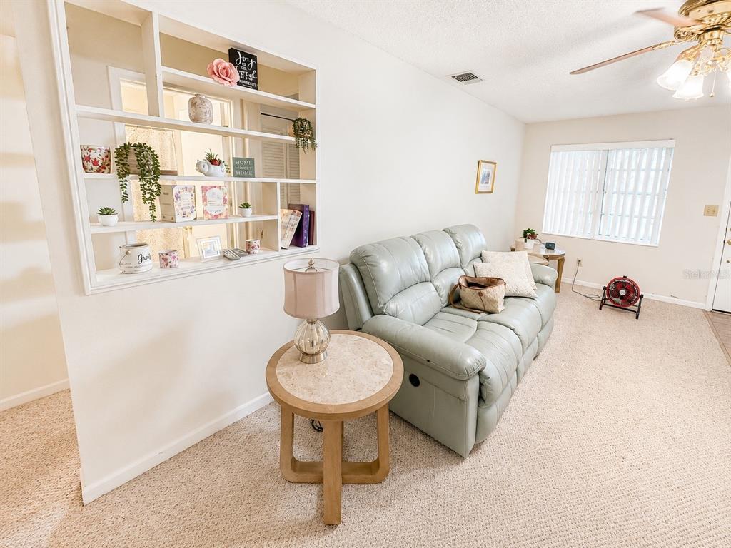 A living room features a light blue sofa, beige carpeting, tile flooring, and a china cabinet — 1131 ORANGE TREE CIRCLE W UNIT C, PALM HARBOR, FL