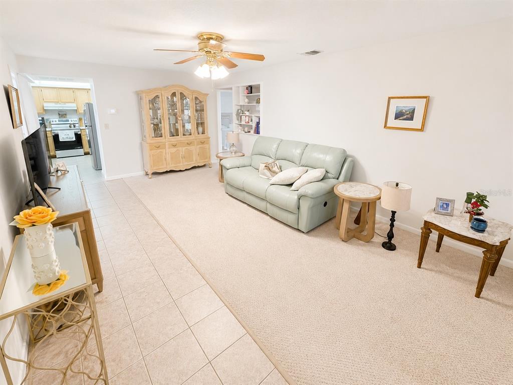 A living room features a light blue reclining sofa, a round side table, and built-in shelving — 1131 ORANGE TREE CIRCLE W UNIT C, PALM HARBOR, FL