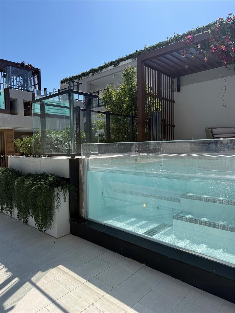 A modern rooftop terrace features a glass-walled swimming pool with built-in steps and a pergola — 20 NE 11th ST # 3212b, Miami FL 33132, MIAMI, FL
