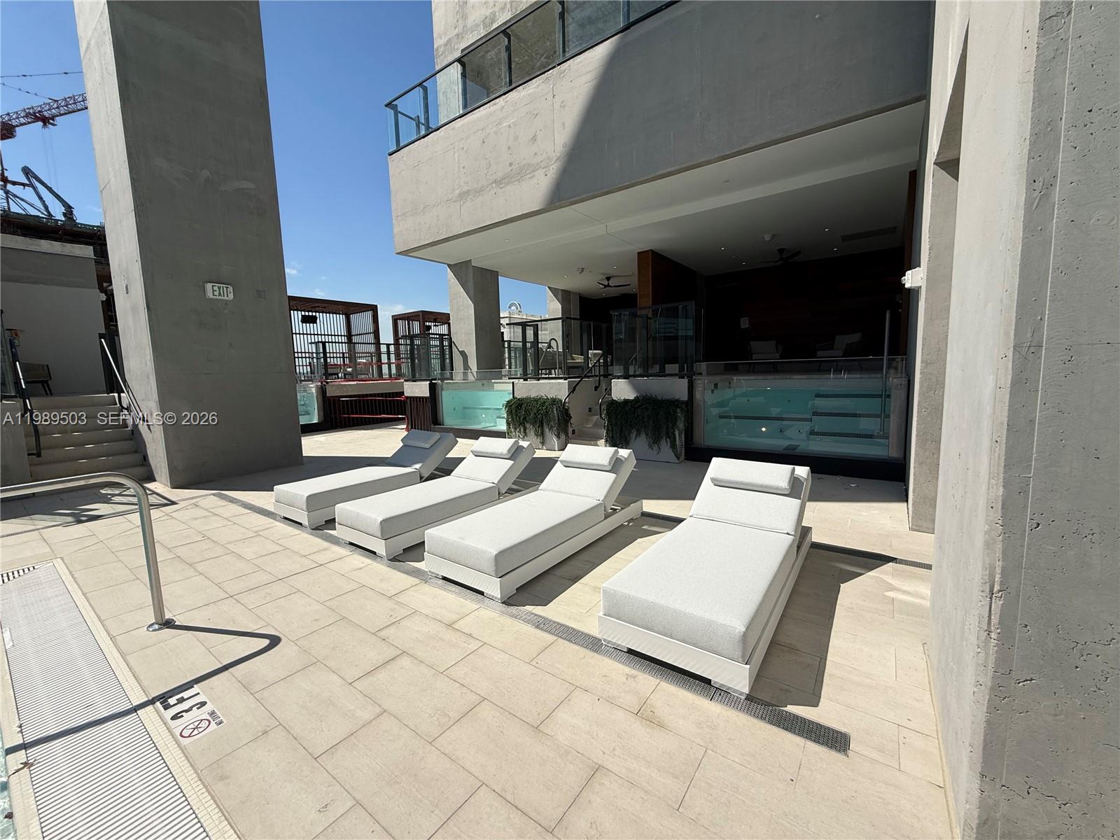 Four white lounge chairs sit on a tiled pool deck near a glass-walled pool — 20 NE 11th ST # 3212b, Miami FL 33132, MIAMI, FL