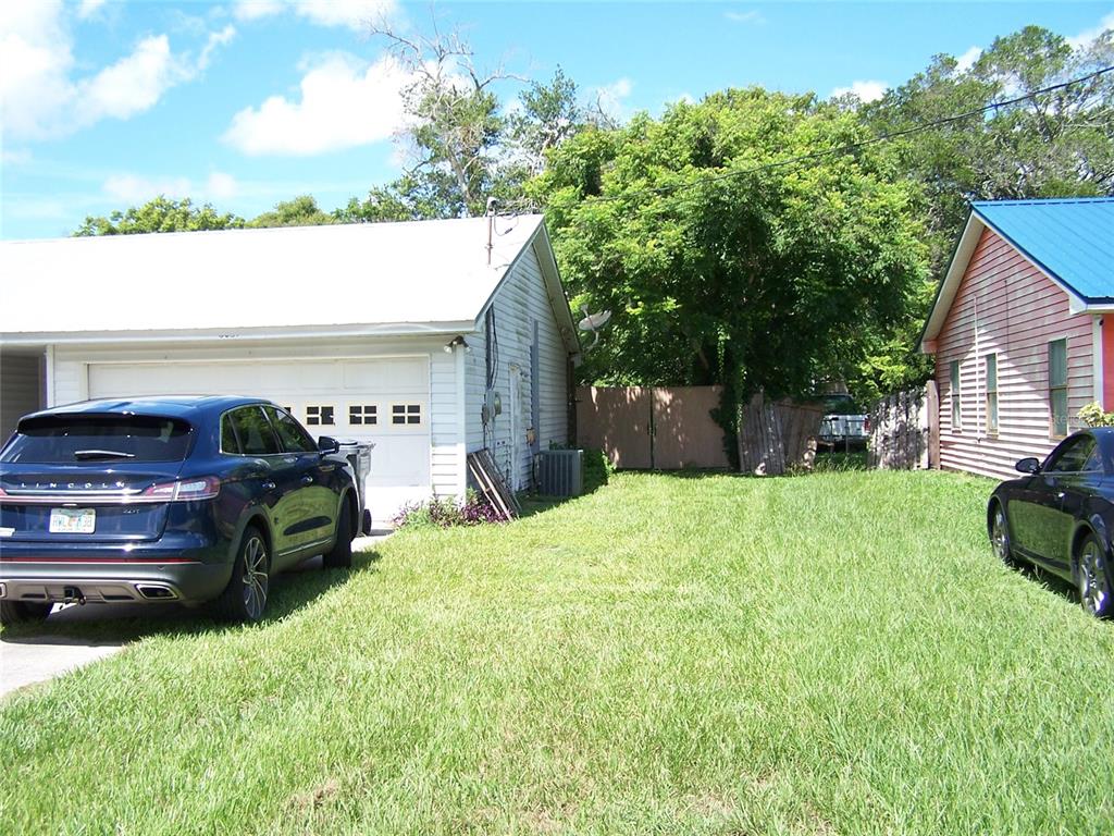 A grassy yard sits between a white garage and a pink house with a blue roof — 6061 STRICKLAND AVENUE, LAKELAND, FL