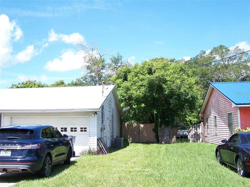 A grassy yard sits between a white garage and a red house under a blue sky — 6061 STRICKLAND AVENUE, LAKELAND, FL
