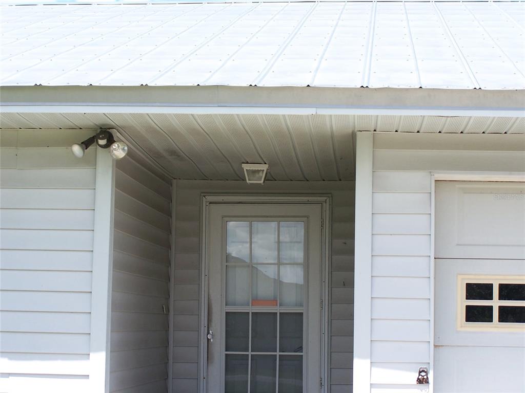 A white-sided house exterior features a metal roof, a storm door, and a porch light — 6061 STRICKLAND AVENUE, LAKELAND, FL