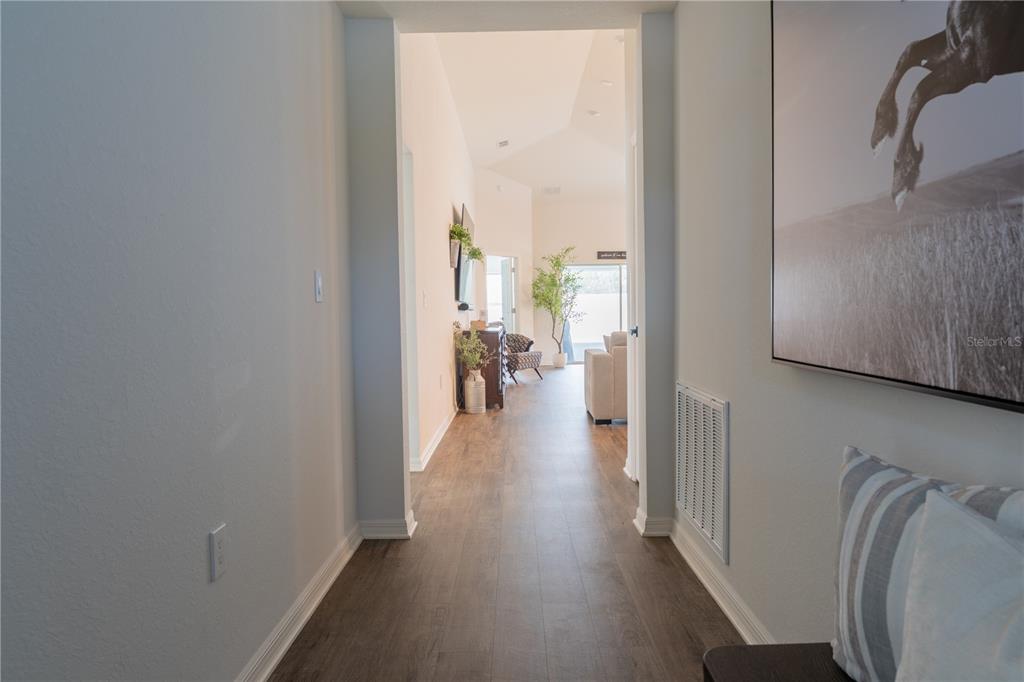 A hallway with wood-look flooring leads toward a living area with vaulted ceilings — 909 MONTGOMERY LANE, POLK CITY, FL