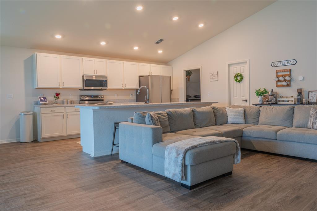 An open-concept kitchen with white cabinets and a gray sectional sofa in the living area — 909 MONTGOMERY LANE, POLK CITY, FL