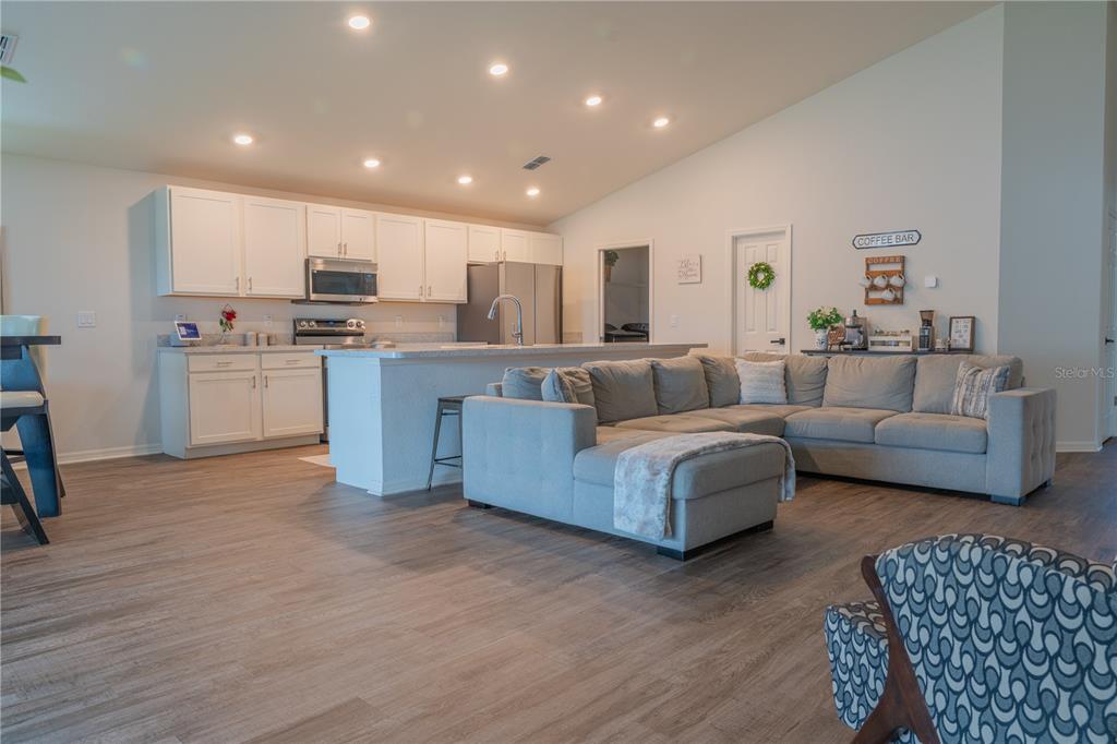 An open-concept kitchen and living area features white cabinetry, a gray sectional, and wood-look flooring — 909 MONTGOMERY LANE, POLK CITY, FL