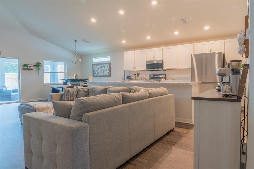 An open-concept living room and kitchen feature light gray furniture, white cabinetry, and wood-look flooring — 909 MONTGOMERY LANE, POLK CITY, FL