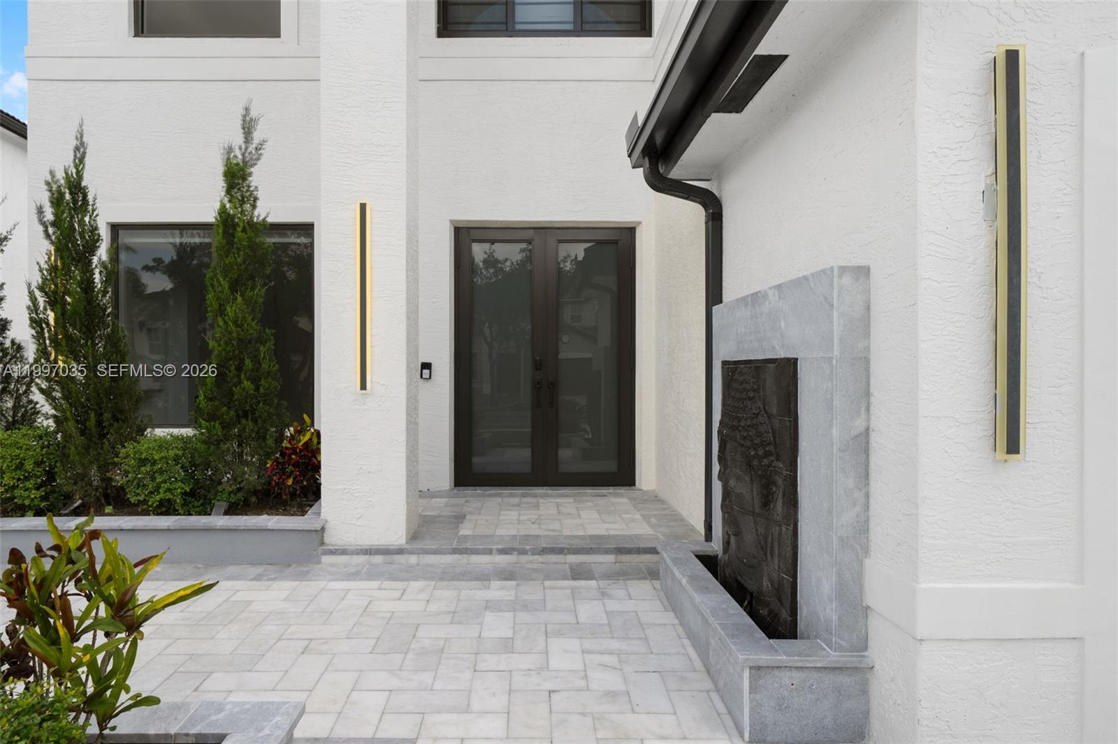 A modern home entrance features a stone water feature, double glass doors, and vertical lighting — 2241 SW 164th Ave, Miramar FL 33027, MIRAMAR, FL