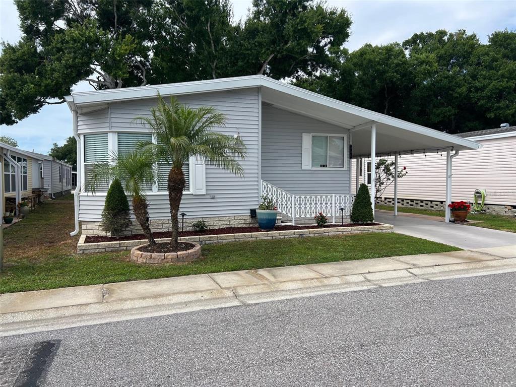 A light gray manufactured home with a carport, palm trees, and a stone-bordered garden bed — 1001 STARKEY ROAD UNIT 331, LARGO, FL