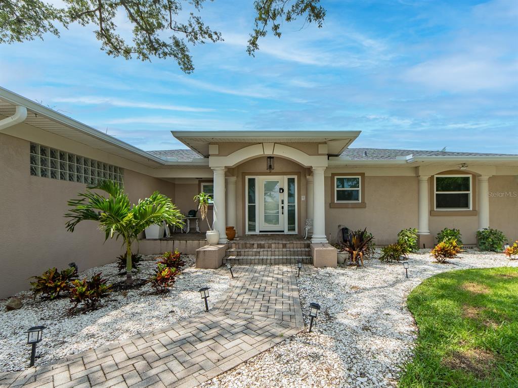 The exterior of a single-story house features a brick walkway leading to a covered entryway — 1826 VENETIAN POINT DRIVE, CLEARWATER, FL