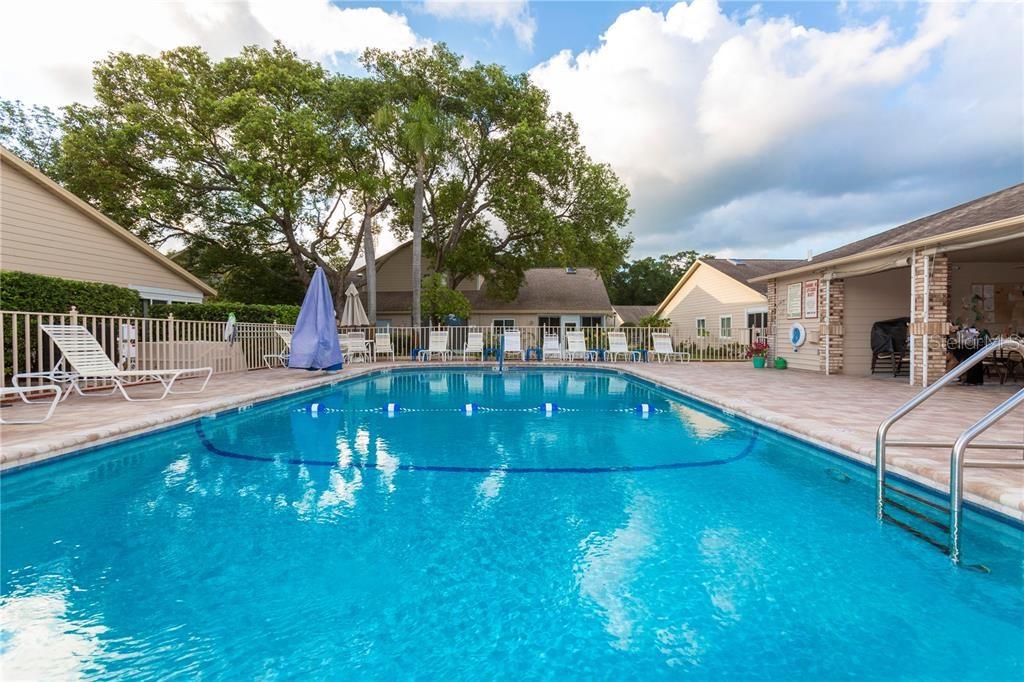 A swimming pool surrounded by a patio, lounge chairs, and residential buildings under a cloudy sky — 4523 GLEN HOLLOW, NEW PORT RICHEY, FL