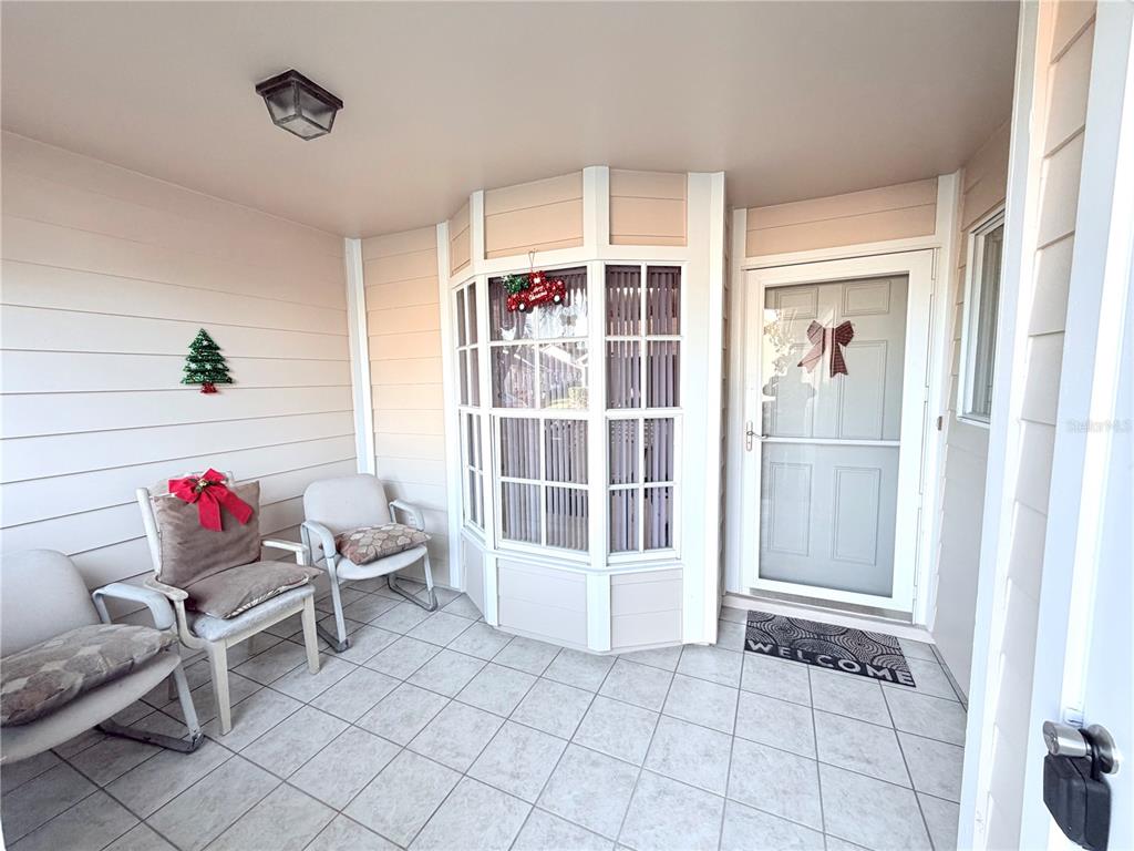A covered porch features tiled flooring, two chairs, a bay window, and a front door — 4523 GLEN HOLLOW, NEW PORT RICHEY, FL