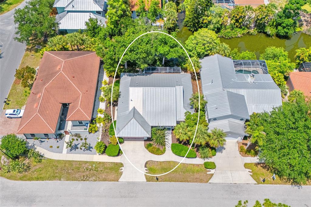 An aerial view shows a house with a metal roof surrounded by trees and landscaping — 400 TORTUGA DRIVE, NOKOMIS, FL