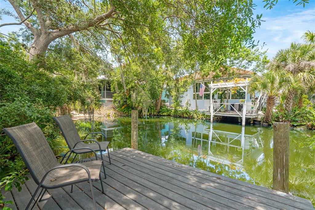 A wooden deck with two chairs overlooks a pond toward a house with a pergola — 400 TORTUGA DRIVE, NOKOMIS, FL