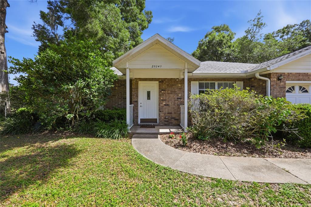 A brick house exterior features a covered front entrance with a white door and walkway — 25249 SW 18TH AVENUE, NEWBERRY, FL