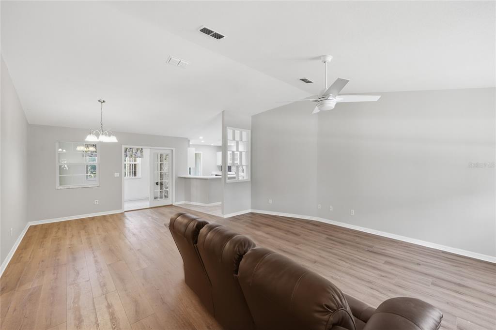 A living room with wood-look flooring, a ceiling fan, and a view into the kitchen — 25249 SW 18TH AVENUE, NEWBERRY, FL