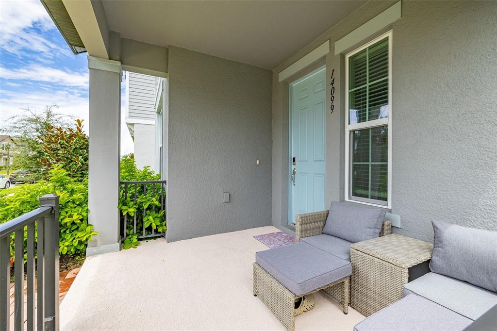 A covered front porch features a light blue door, gray stucco walls, and wicker patio furniture — 14099 FRASIER STREET, WINTER GARDEN, FL