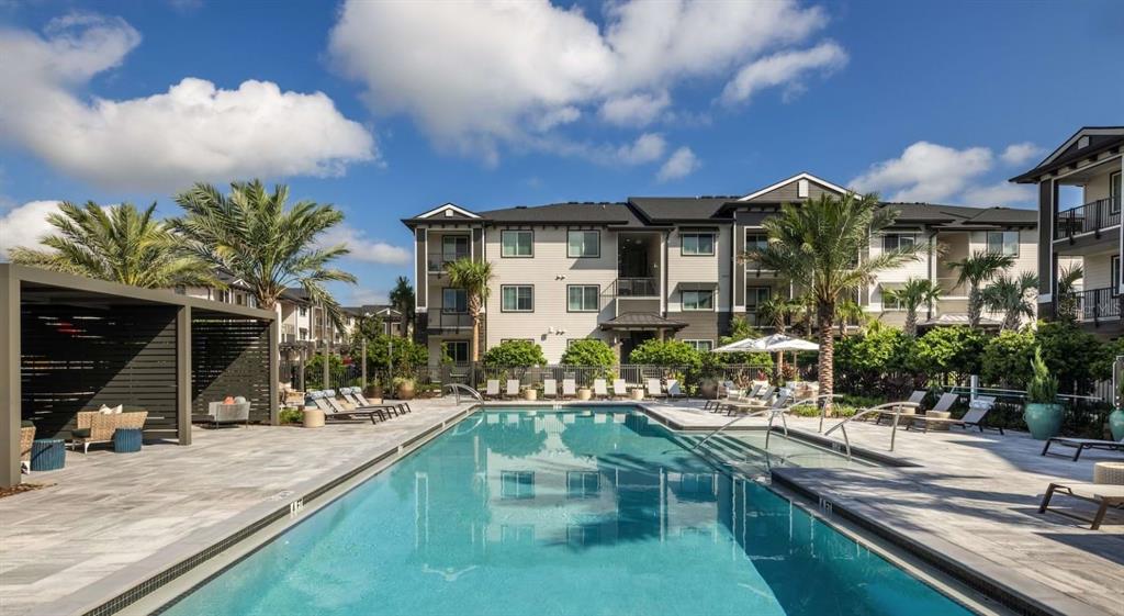 A rectangular swimming pool sits in front of a multi-story apartment building with palm trees — 5000 COLLINA TERRACE UNIT B1, CLERMONT, FL