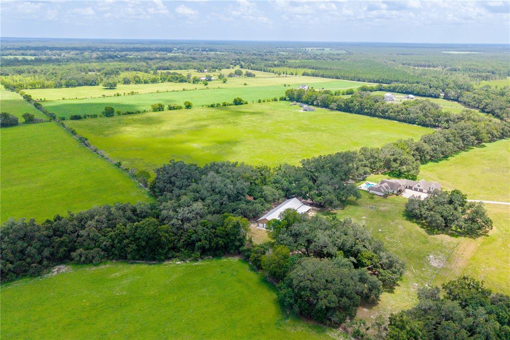An aerial view shows a rural property with a house, outbuilding, and expansive green pastures — 000 SW STATE ROAD 45, NEWBERRY, FL