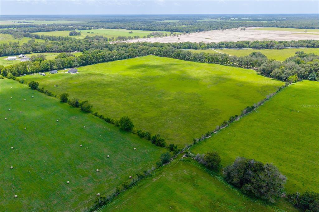 An aerial view shows a large, open green pasture bordered by trees and rural structures — 000 SW STATE ROAD 45, NEWBERRY, FL