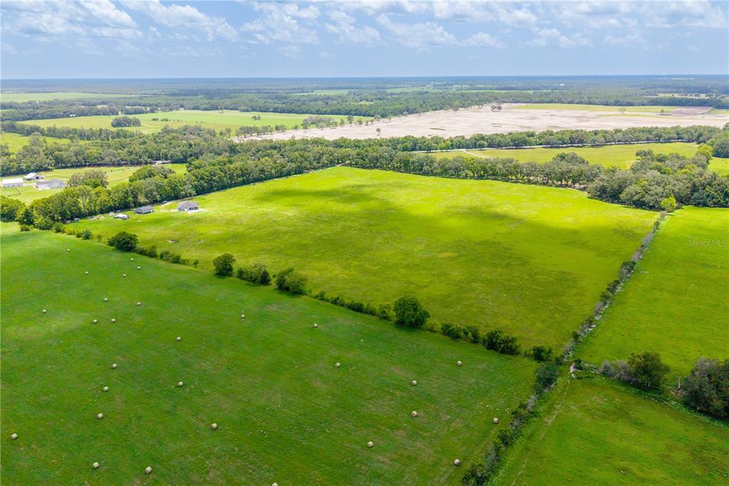 An aerial view shows a large, open green pasture with scattered hay bales and trees — 000 SW STATE ROAD 45, NEWBERRY, FL