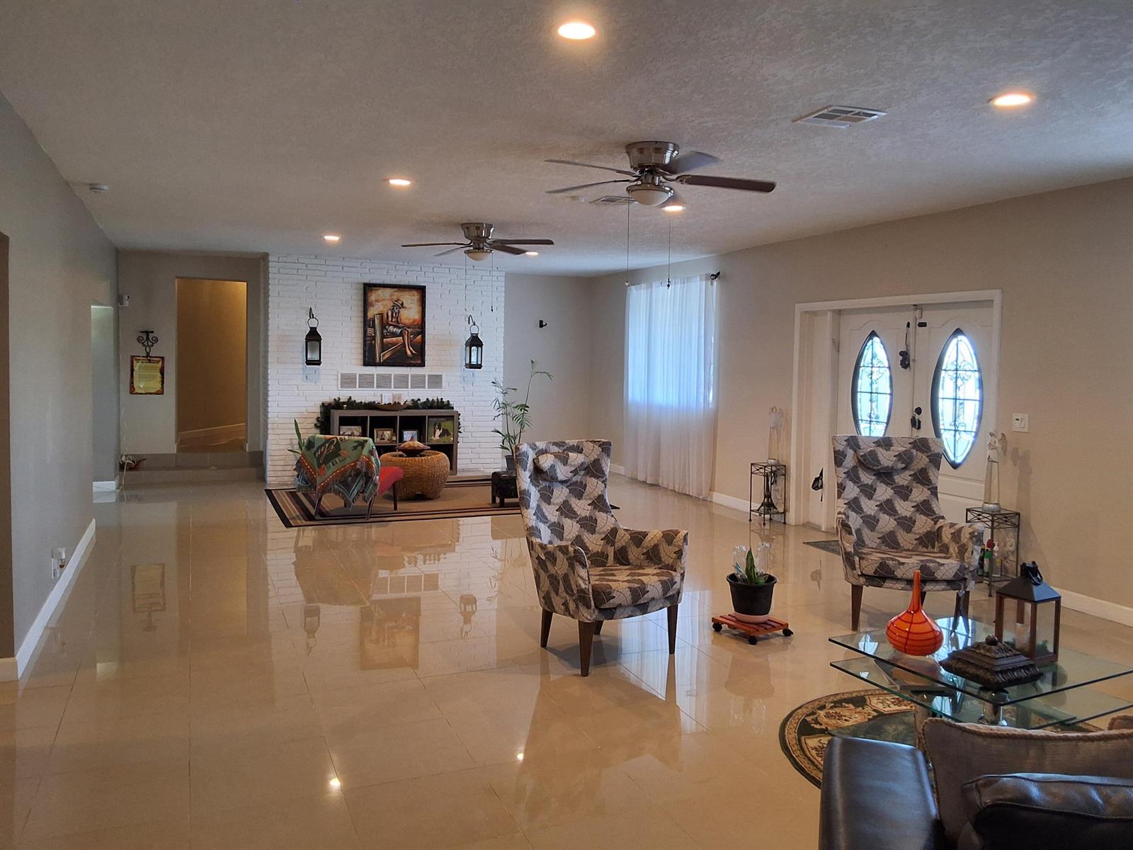 A spacious living room features tile flooring, two ceiling fans, and a white brick fireplace — 1221 Bacom Point Road, Pahokee FL 33476, PAHOKEE, FL
