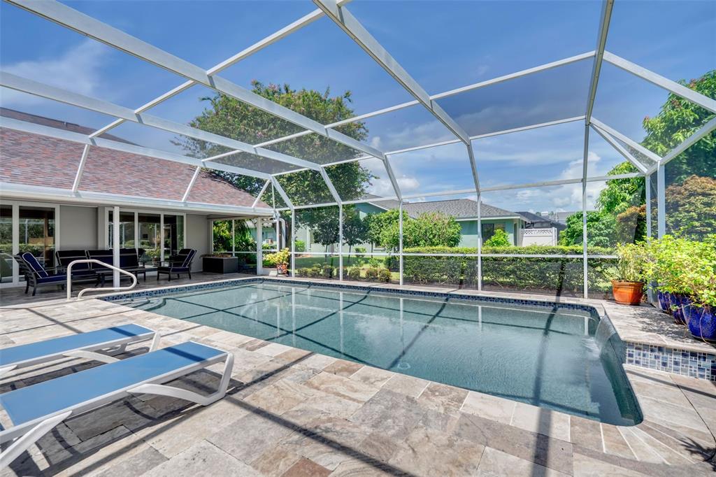 A screened-in swimming pool with stone decking and lounge chairs sits behind a residential home — 4528 SPRING FLOWER COURT, SARASOTA, FL