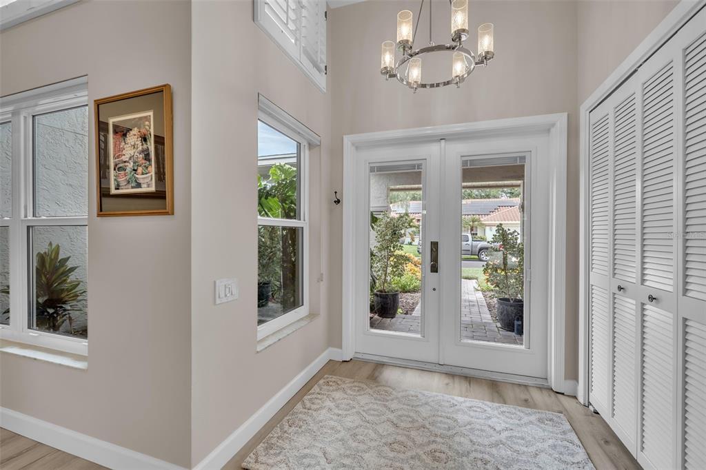 An entryway features double glass doors, a chandelier, light-colored walls, and white louvered closet doors — 4528 SPRING FLOWER COURT, SARASOTA, FL