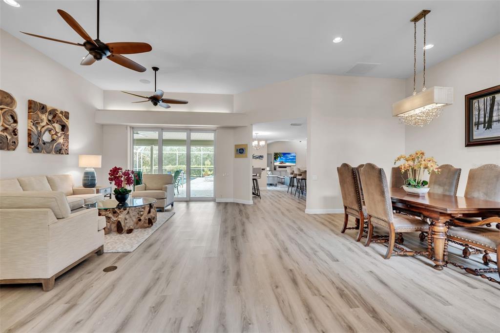 An open-concept living and dining area features light wood flooring and two ceiling fans — 4528 SPRING FLOWER COURT, SARASOTA, FL