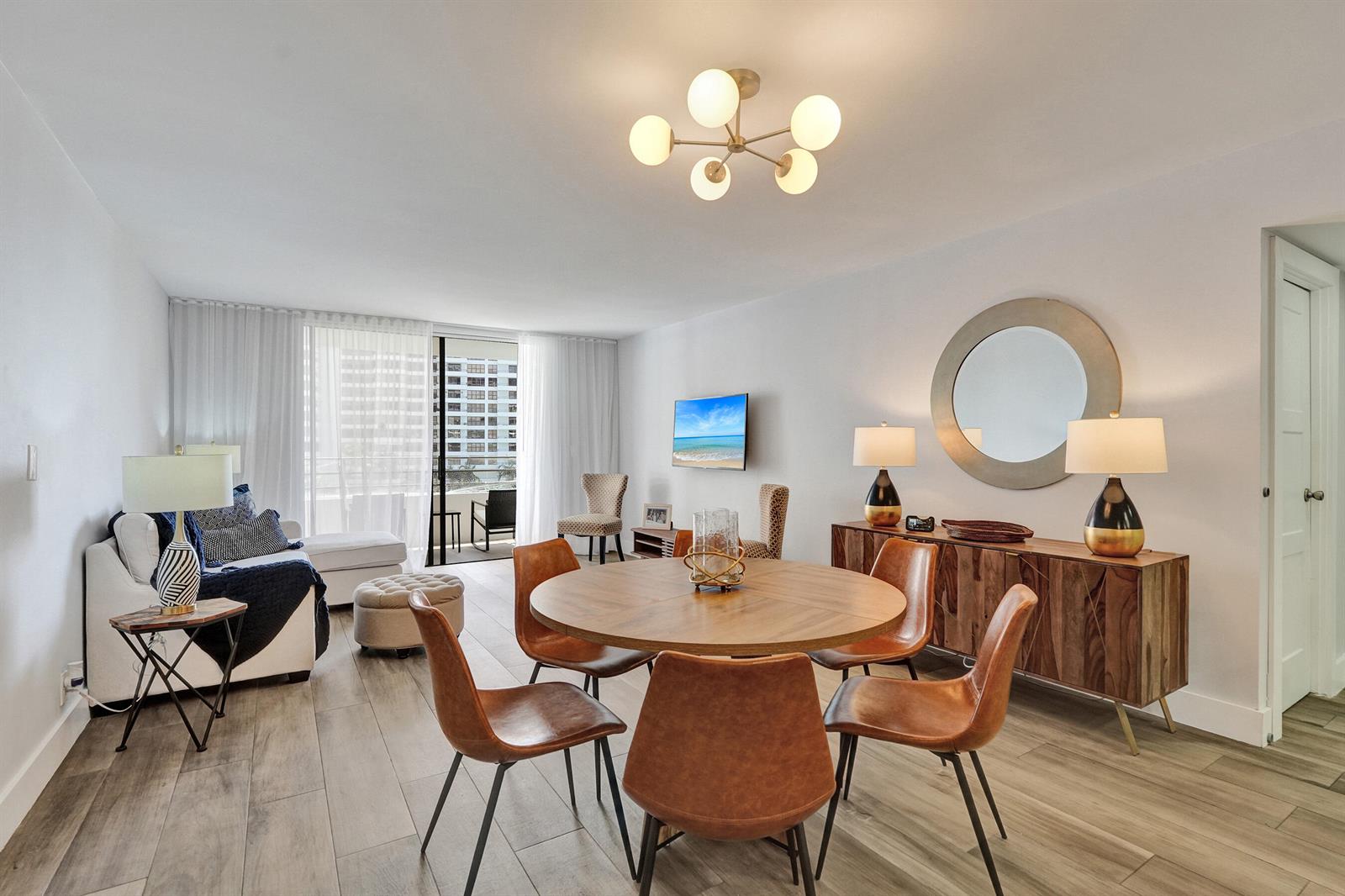 A living and dining room features a round wooden table, leather chairs, and a balcony — 600 Three Islands Boulevard # 615, Hallandale Beach FL 33009, HALLANDALE BEACH, FL