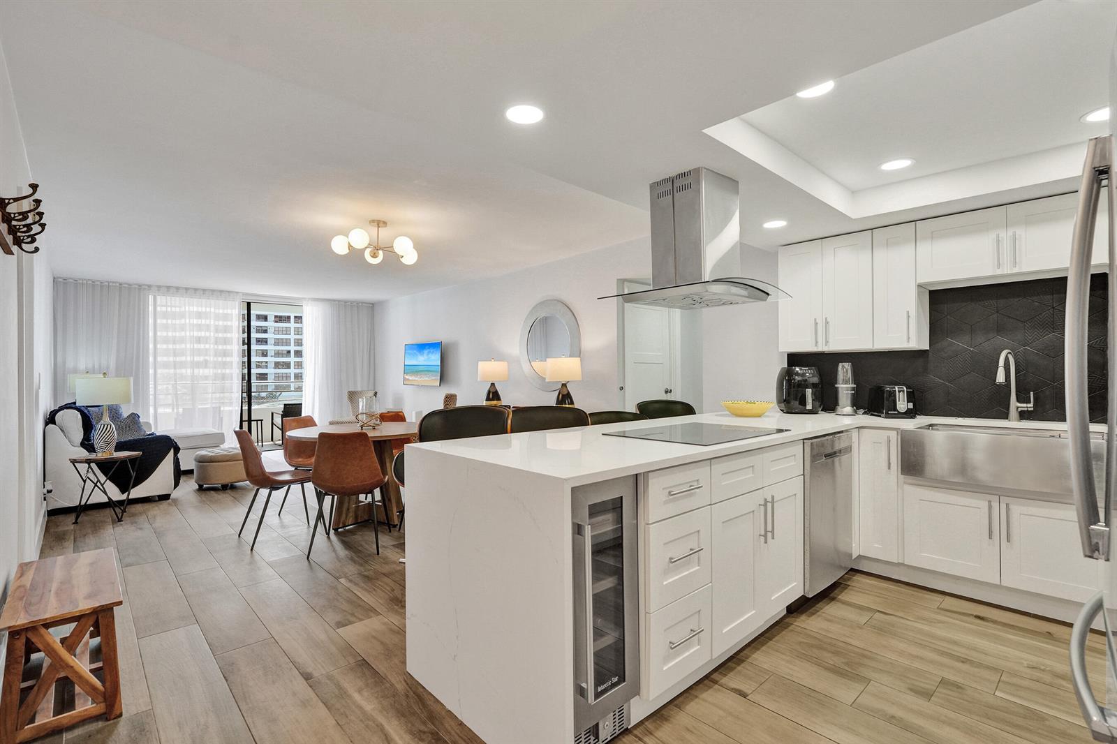 A modern open-concept kitchen and dining area features white cabinetry, a quartz island, and wood-look flooring — 600 Three Islands Boulevard # 615, Hallandale Beach FL 33009, HALLANDALE BEACH, FL