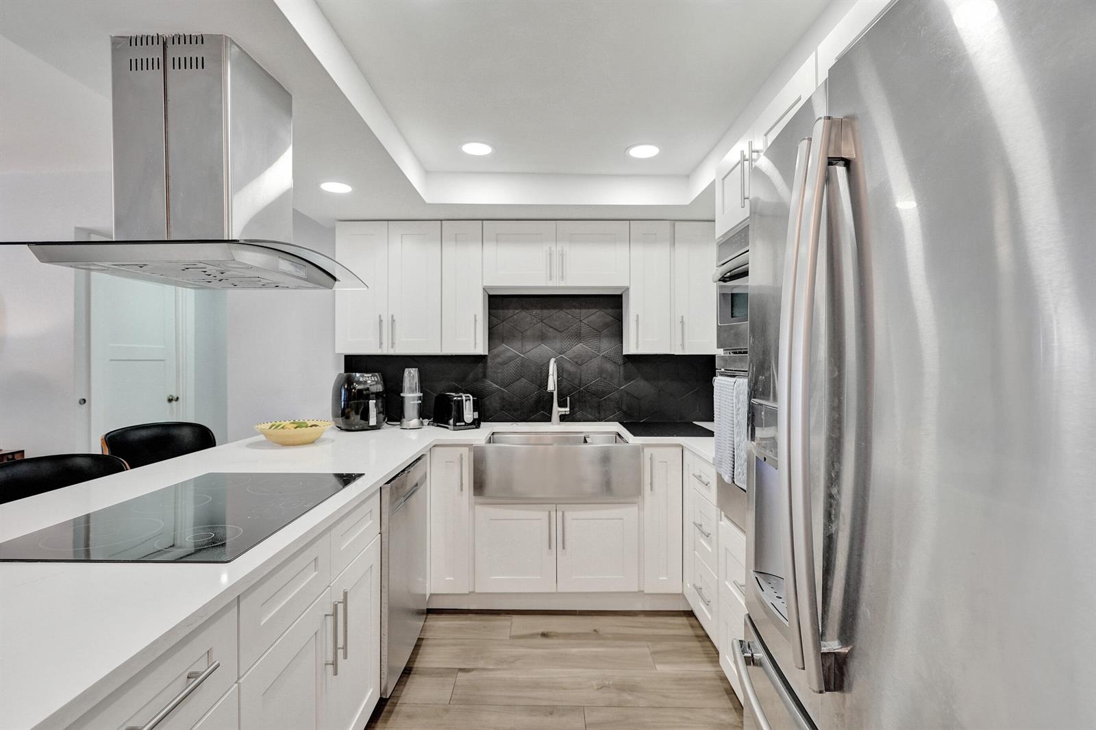 A modern kitchen features white cabinets, stainless steel appliances, a farmhouse sink, and black backsplash — 600 Three Islands Boulevard # 615, Hallandale Beach FL 33009, HALLANDALE BEACH, FL