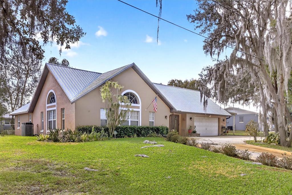 A single-story house with a metal roof, beige stucco siding, and a two-car garage — 2725 W CHARING ROAD, AVON PARK, FL