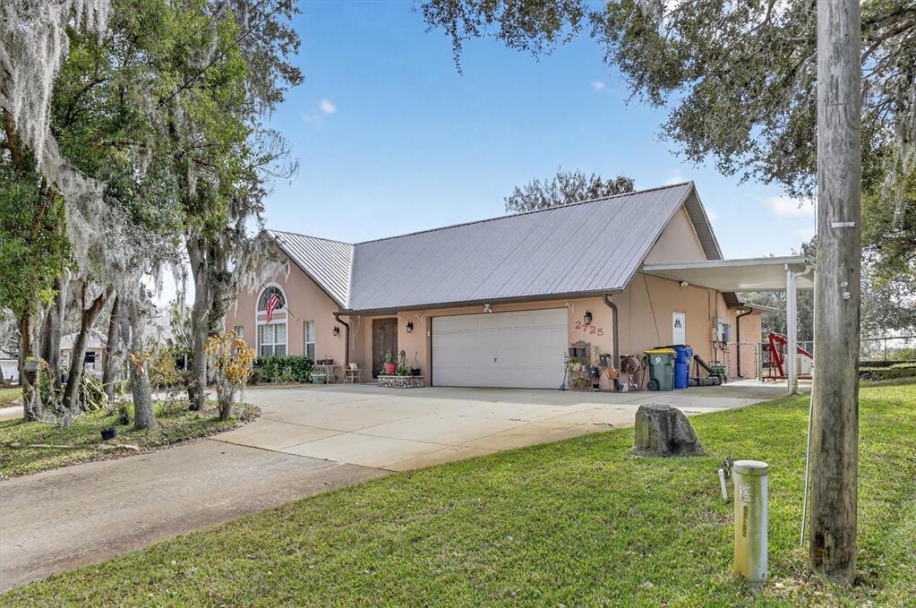 A single-story house with a metal roof, a two-car garage, and a side carport — 2725 W CHARING ROAD, AVON PARK, FL