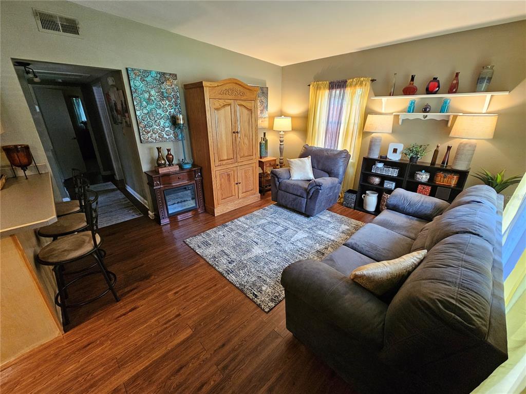 A living room features a grey sofa, an armchair, wood flooring, and a fireplace console — 1908 WEEKS AVENUE, ORLANDO, FL