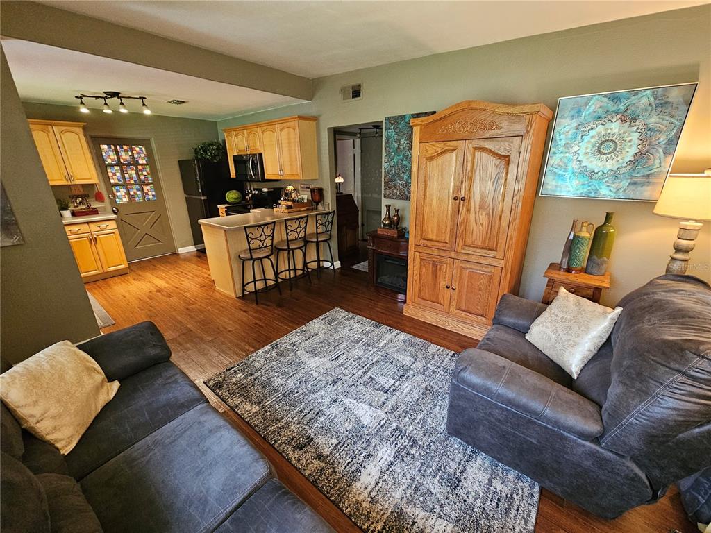 A living room with a gray sofa and rug opens into a kitchen with wooden cabinets — 1908 WEEKS AVENUE, ORLANDO, FL