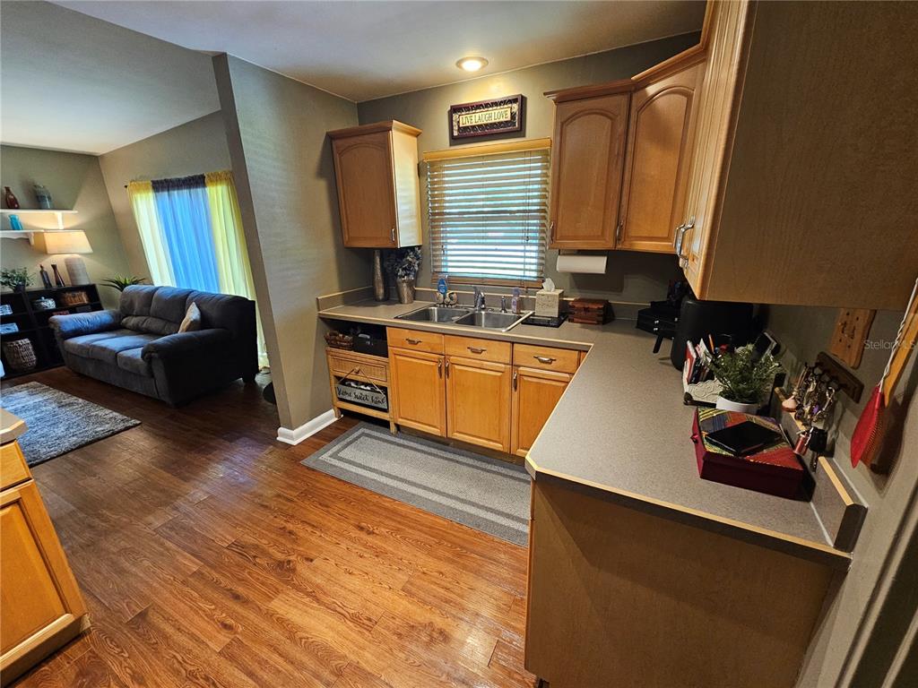 A kitchen with wood cabinets and gray countertops opens into a living room with wood floors — 1908 WEEKS AVENUE, ORLANDO, FL