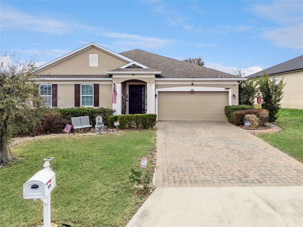 A single-story suburban house features a tan stucco exterior, a paved driveway, and a garage — 9889 LENOX STREET, CLERMONT, FL