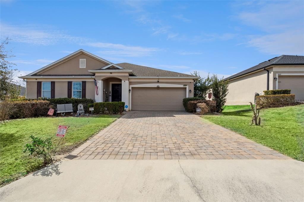 A single-story house with a tan stucco exterior, a paved driveway, and a two-car garage — 9889 LENOX STREET, CLERMONT, FL
