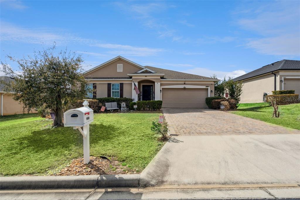 A single-story suburban house with a tan stucco exterior, a paved driveway, and a lawn — 9889 LENOX STREET, CLERMONT, FL
