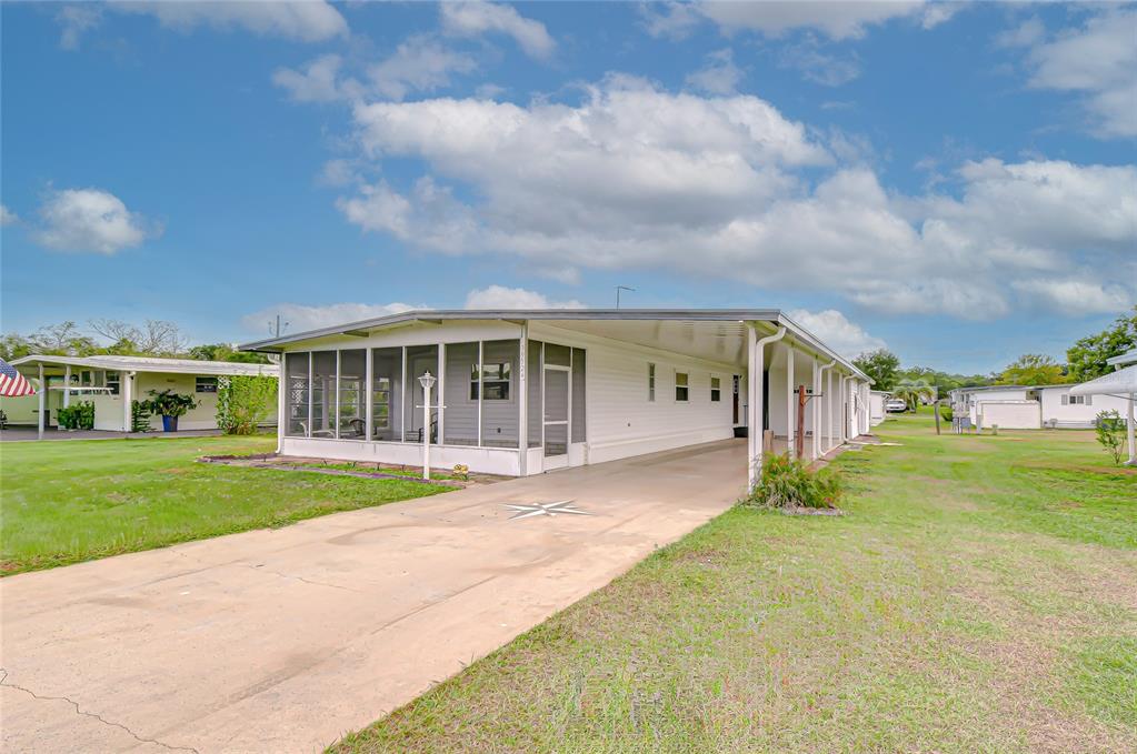 A white mobile home features a screened-in front porch and an attached covered carport — 39524 DUNDEE ROAD, ZEPHYRHILLS, FL