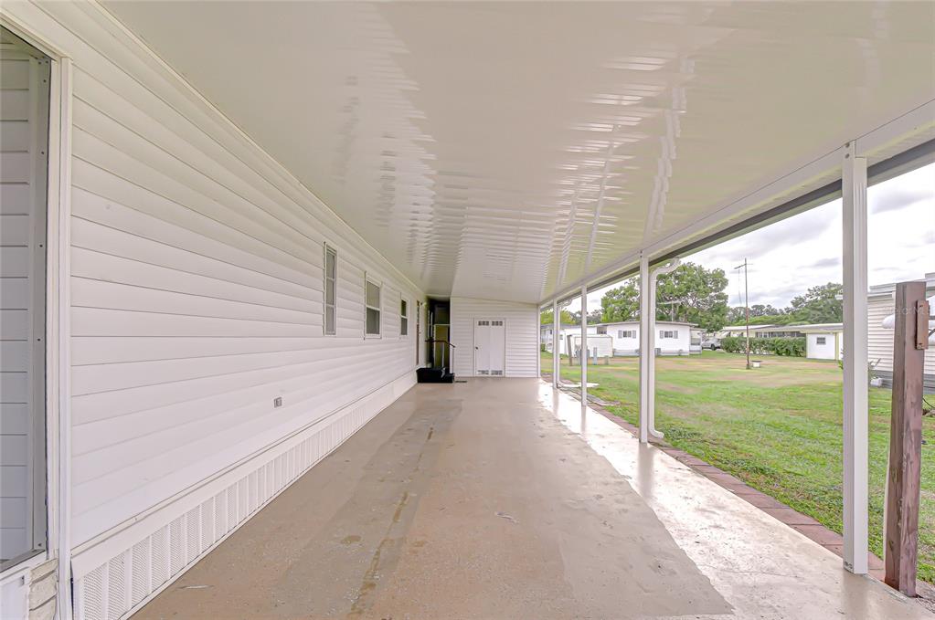 A long, covered concrete carport runs alongside the white siding of a mobile home — 39524 DUNDEE ROAD, ZEPHYRHILLS, FL
