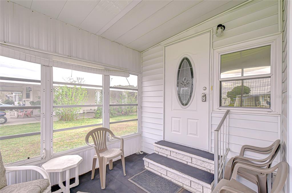 A screened-in porch features a white front door, two steps, and several plastic chairs — 39524 DUNDEE ROAD, ZEPHYRHILLS, FL