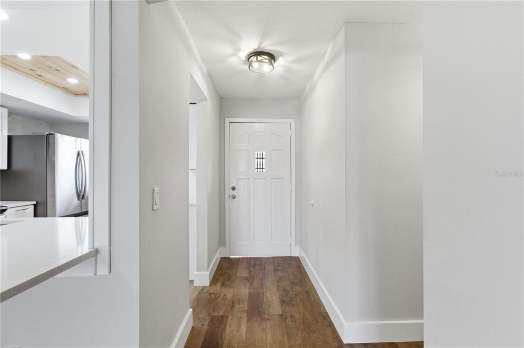 A hallway with wood-look flooring leads to a white front door under a ceiling light — 3500 BENEVA ROAD UNIT 307, SARASOTA, FL