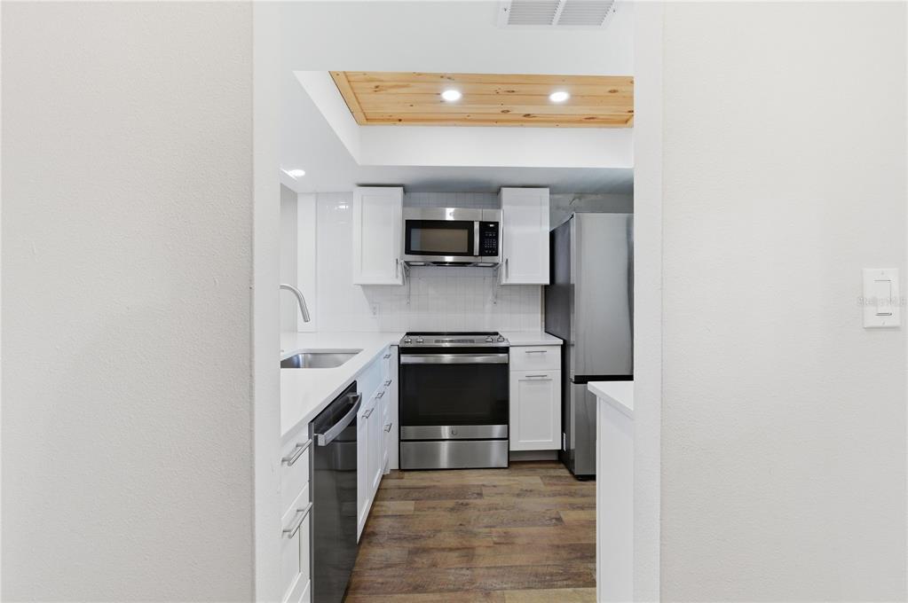 A galley kitchen features white cabinets, stainless steel appliances, and a wood-paneled ceiling accent — 3500 BENEVA ROAD UNIT 307, SARASOTA, FL