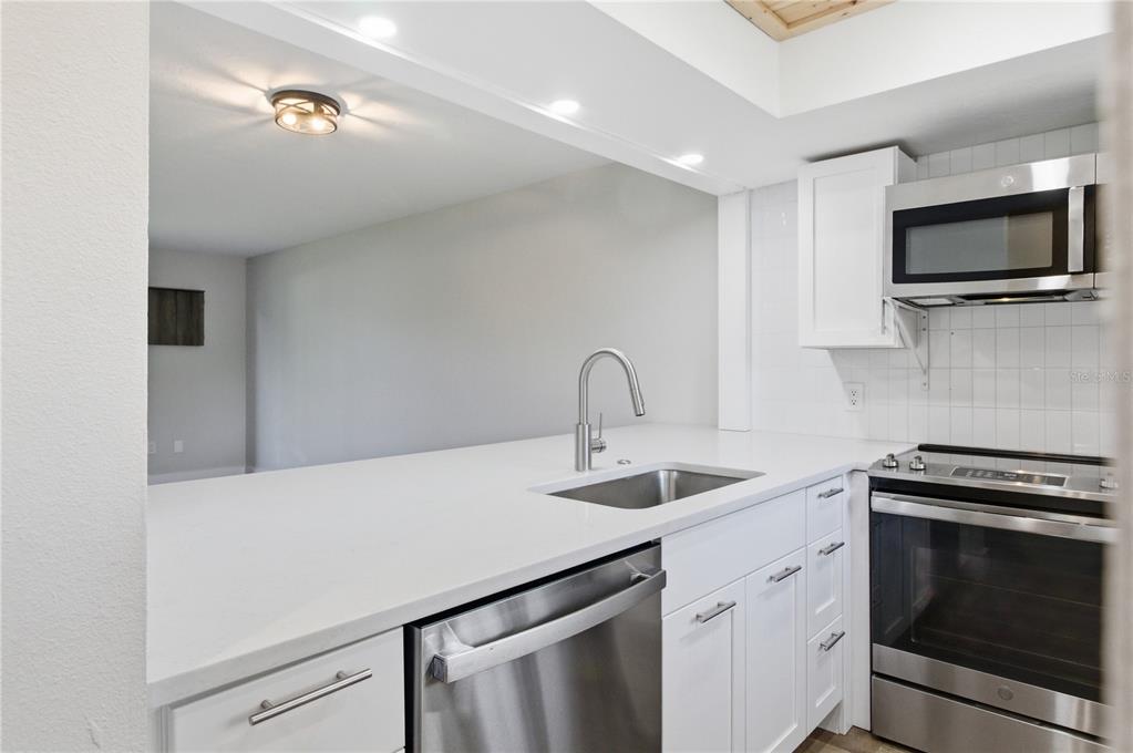 A modern kitchen features white cabinets, stainless steel appliances, and a white quartz countertop — 3500 BENEVA ROAD UNIT 307, SARASOTA, FL
