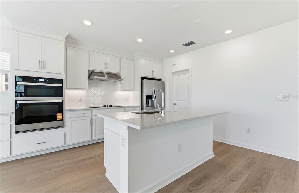 A modern kitchen features white cabinetry, stainless steel appliances, a center island, and wood flooring — 7910 PALM PARADISE PLACE, PARRISH, FL