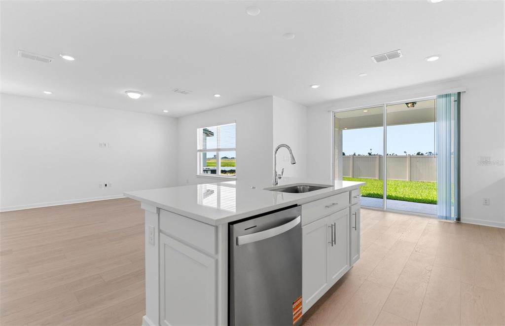 A kitchen island with a stainless steel dishwasher faces a living area and sliding glass doors — 7910 PALM PARADISE PLACE, PARRISH, FL