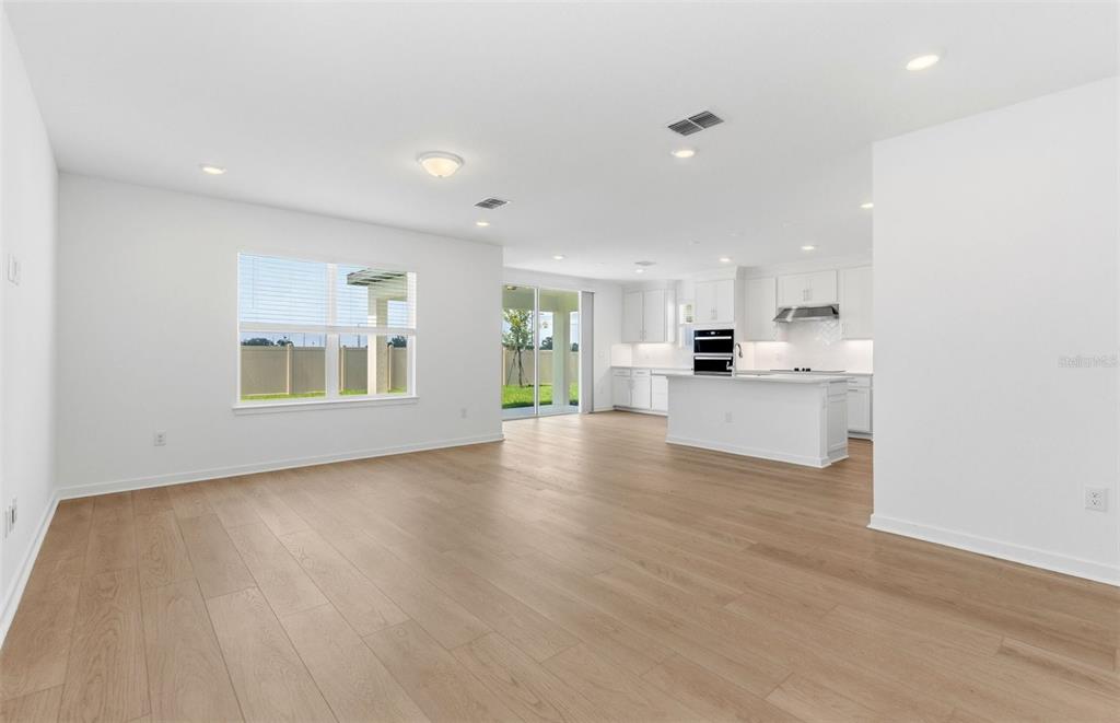 An open-concept living room and kitchen with white cabinetry, light wood flooring, and sliding doors — 7910 PALM PARADISE PLACE, PARRISH, FL